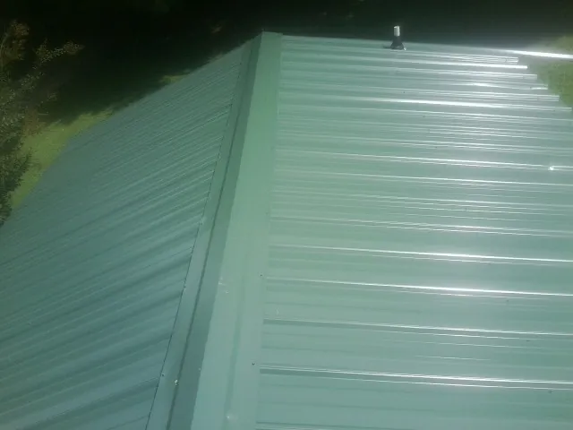 New green metal panels meeting at the ridge of a roof — Flat Roof Repair work by our crew in Forest City