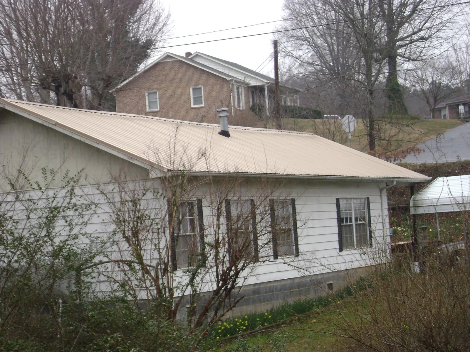 Tan metal roof on a white sided house set into a hillside — Commercial Roofing by Roofing Brothers in Forest City